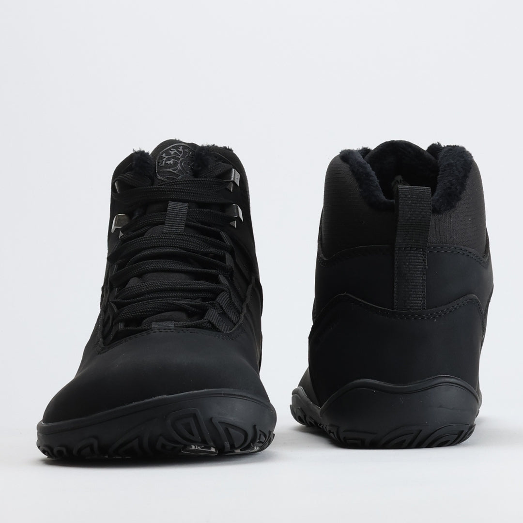 Noenmusta Vaistoa Uoma Talvi 3 -paljasjalkavaelluskenkäpari kuvattuna edestä ja takaa. Kuvassa näkyy leveä varvastila ja lämmin karvavuori.