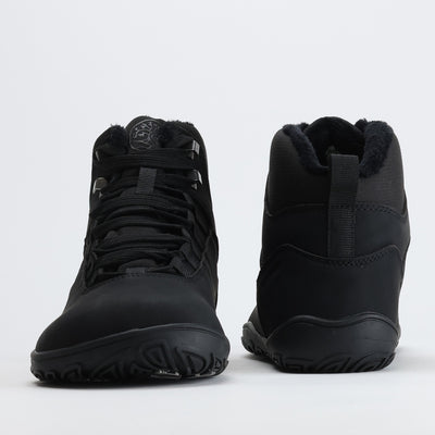 Noenmusta Vaistoa Uoma Talvi 3 -paljasjalkavaelluskenkäpari kuvattuna edestä ja takaa. Kuvassa näkyy leveä varvastila ja lämmin karvavuori.