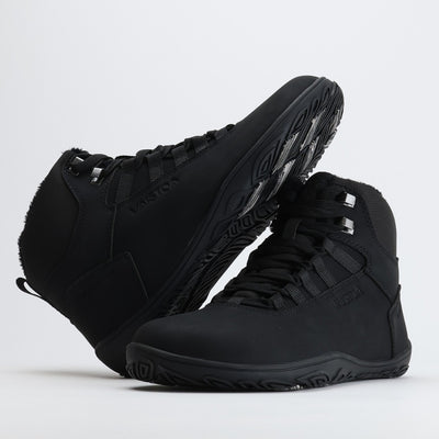 Noenmusta Vaistoa Uoma Talvi 3 -kenkäpari, jossa toinen kenkä nojaa toiseen ja näkyvissä on talvipohjan kitkapalat ja kuviointi.