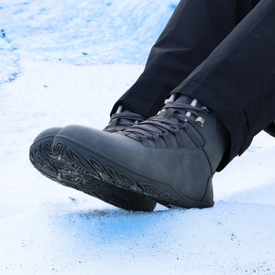 Käyttökuva, jossa henkilö istuu lumisella rinteellä ja kengät näkyvät läheltä. Kuvassa korostuu kengän luonnollinen muoto ja pohjan joustavuus.