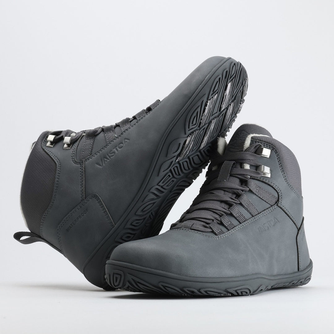 Pakkasharmaa Vaistoa Uoma Talvi 3 -kenkäpari kuvattuna siten, että toinen kenkä nojaa toiseen ja pohjan kitkapalat näkyvät selkeästi.