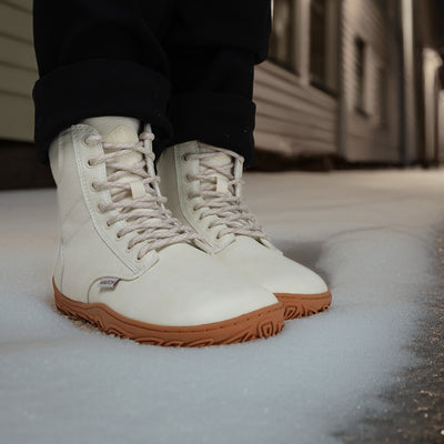 Luonnonvalkeat Vaistoa Hurmos 2 -paljasjalkamaiharit käytössä iltavalaistulla kadulla. Henkilö seisoo lumella rakennusten välissä, kengät korostuvat lämpimässä valossa.