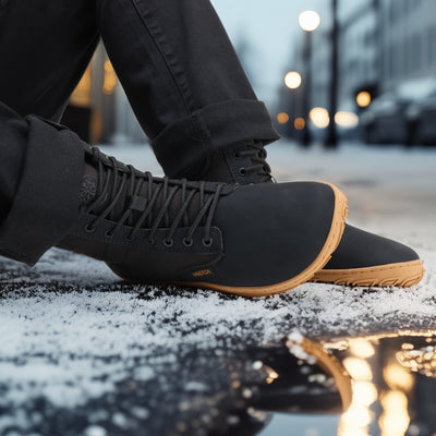 Musta Vaistoa Hurmos 2 -paljasjalkamaiharipari jalassa iltakuvassa. Henkilö istuu kaupungin kadulla lumen ja katuvalojen loisteessa.