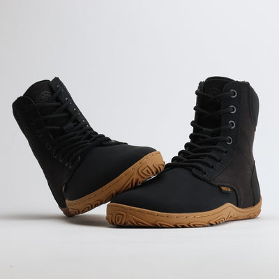 Musta Vaistoa Hurmos 2 -paljasjalkamaiharipari kuvattuna, toinen kenkä nojaa varvastilaan. Kuvakulma korostaa kengän luonnollista muotoa ja pitävää pohjaa.