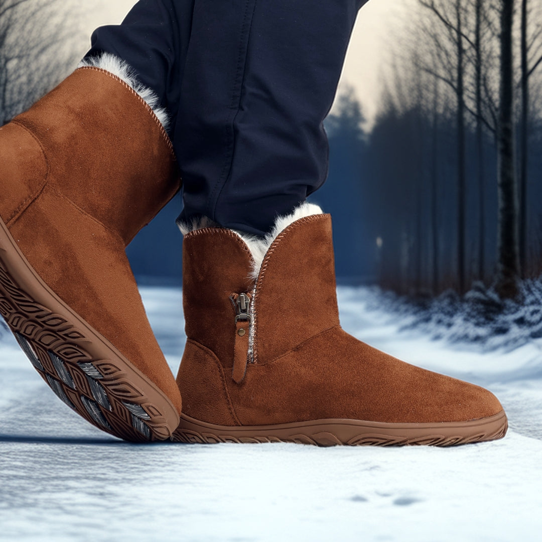 Vaistoa Huurre – paljasjalkabootsit talveen, väri karamellinruskea. Käyttökuva etuviistosta: henkilö kävelee lumisella tiellä Huurre-bootsit jalassa – kuva korostaa lämpöä, joustavuutta ja pitävää pohjaa.