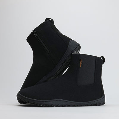 Kaksi samettisen mustaa Vaistoa Sulo -huopanilkkuria seisovat vierekkäin valkoisella taustalla. Toinen kenkä nojaa toisen varteen, paljastaen joustavan Vaistoa Pitoa™ -talvipohjan ja minimalistisen muotoilun. Kuvan oikeassa yläkulmassa näkyy Design from Finland -merkki, joka kertoo kotimaisesta suunnittelusta.